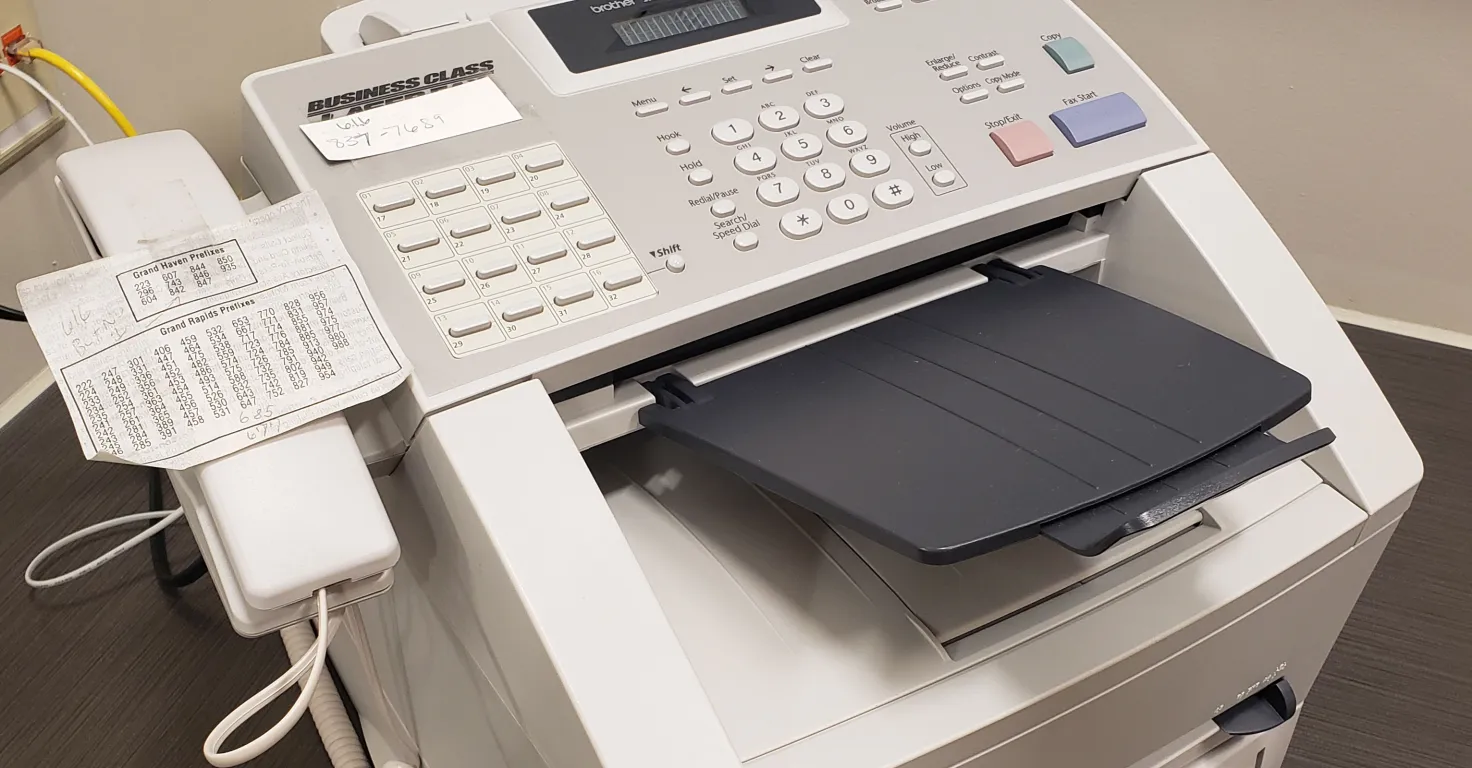 A multifunction printer or fax machine with a document on its tray and cable attachments.