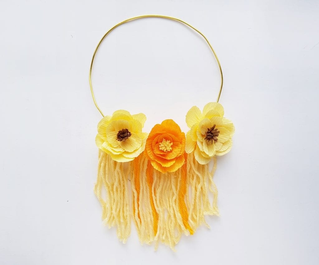 A floral wall hanging with yellow tassel details on a white background.