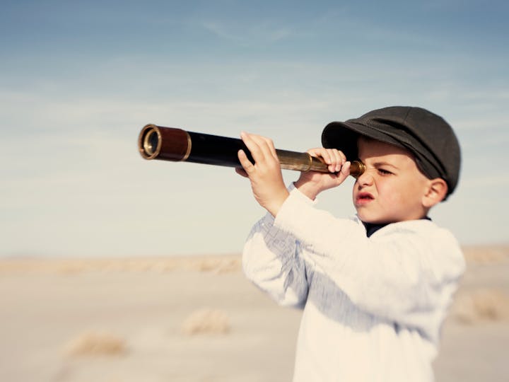 A child in a cap looking through a telescope outdoors.