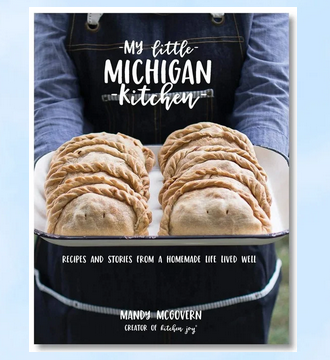 Cookbook cover titled "My Little Michigan Kitchen" with several pasties being held.