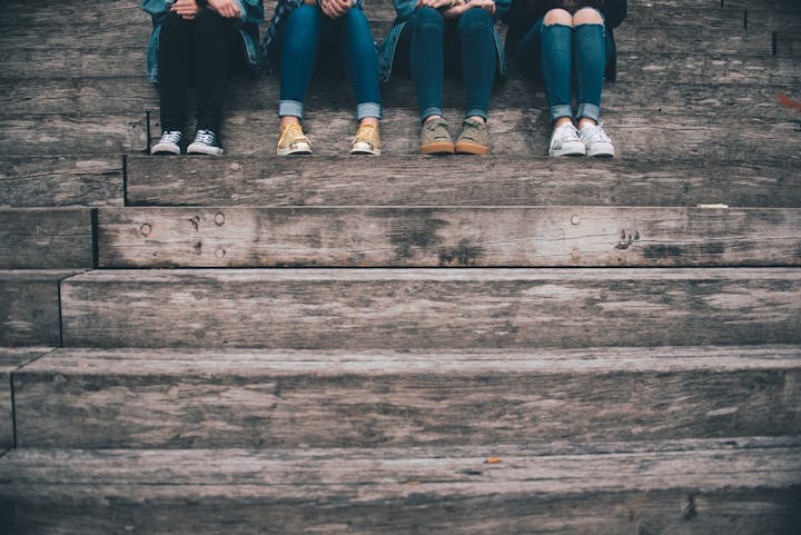 Four pairs of legs with various shoes sitting on wooden steps.