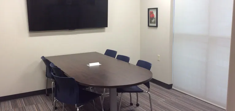 A modern conference room with a table, chairs, TV, and artwork on the wall.