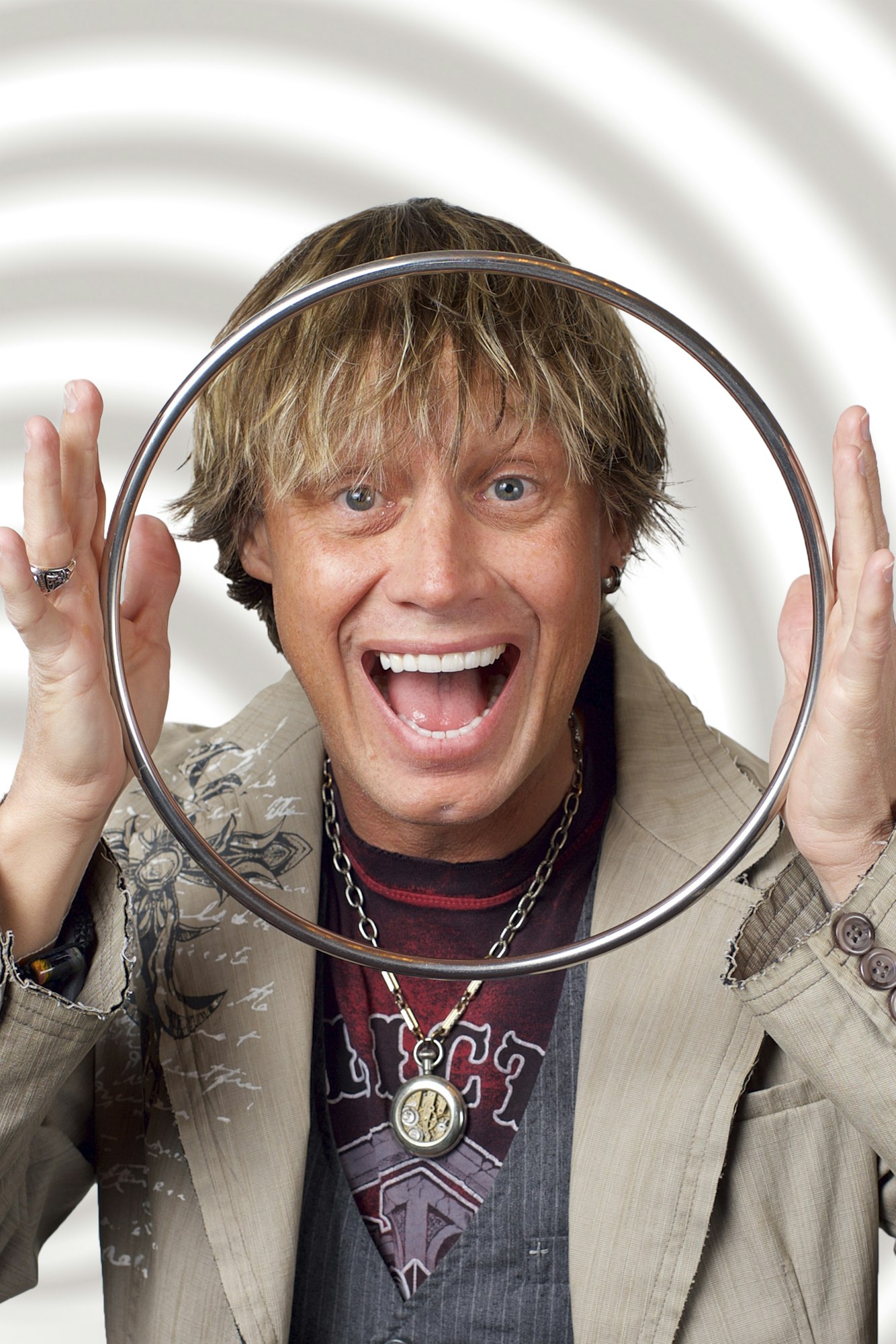 A person smiling and holding a metal ring with a patterned background.