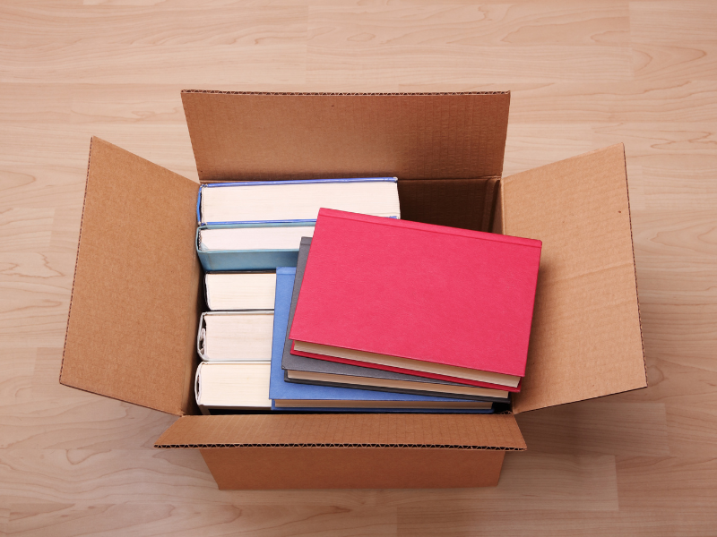 A cardboard box filled with books on a wooden floor.