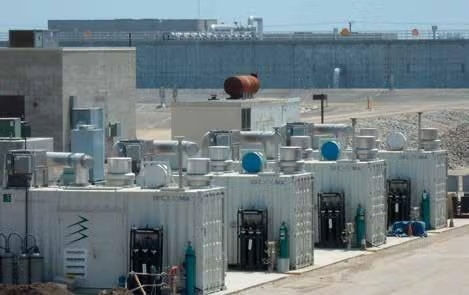 Industrial facility with multiple large containers and equipment, possibly for energy or waste processing, under clear blue sky.