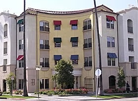 A four-story building with colorful awnings, palm trees, and landscaped greenery in front.