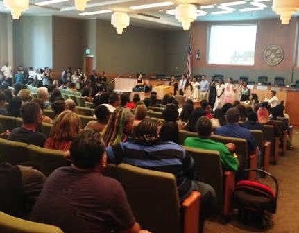 A group of people are gathered in a conference room, with some standing at the front speaking to an audience seated in rows.