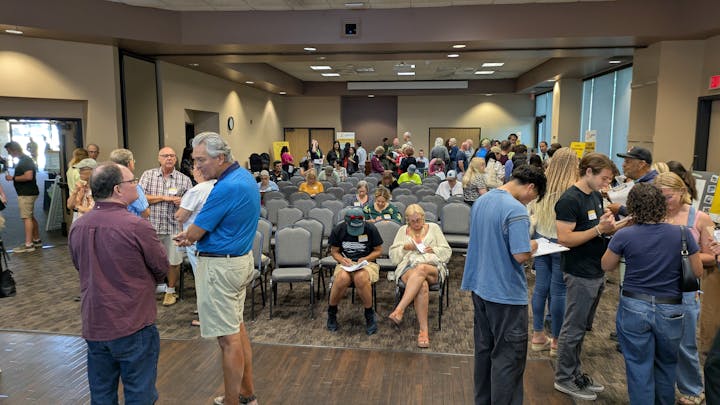 A crowded event where people are mingling and seated, possibly for a meeting or community gathering.