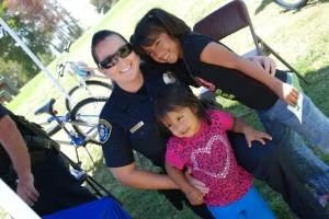 A police officer smiles with two young girls outdoors, near bicycles.