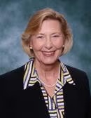 Portrait of a smiling woman with blond hair wearing a striped blazer over a collared shirt.