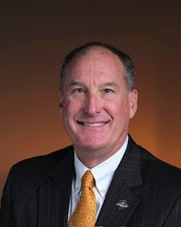 A man in a suit and tie smiling against a brown background.