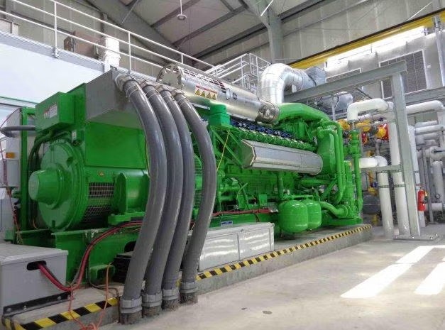 Large green industrial machine with multiple pipes, likely a generator or engine, in a factory setting.
