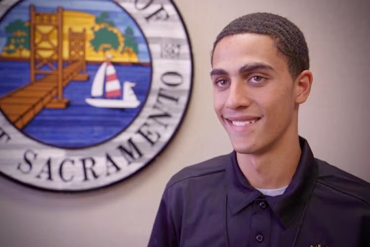 A person smiling in front of the Sacramento city seal.