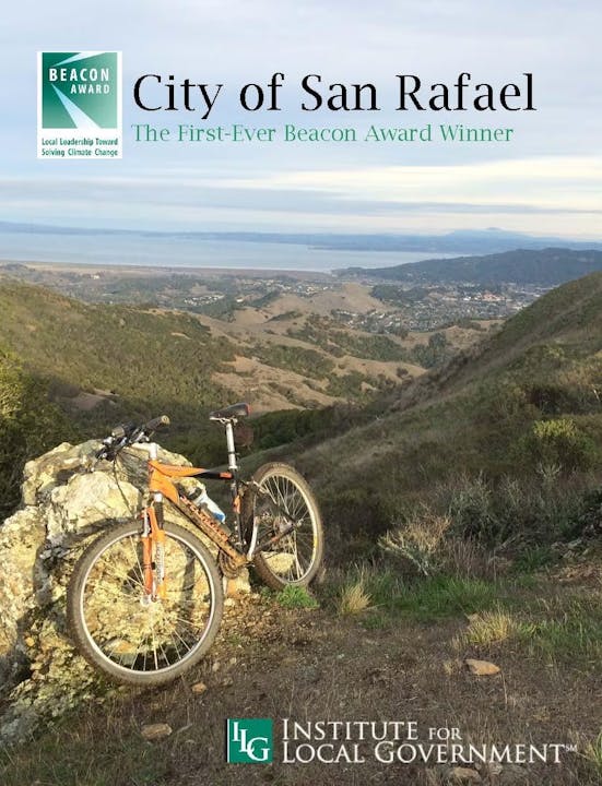 A mountain bike on a hillside with a view of a city and text about San Rafael winning a Beacon Award.