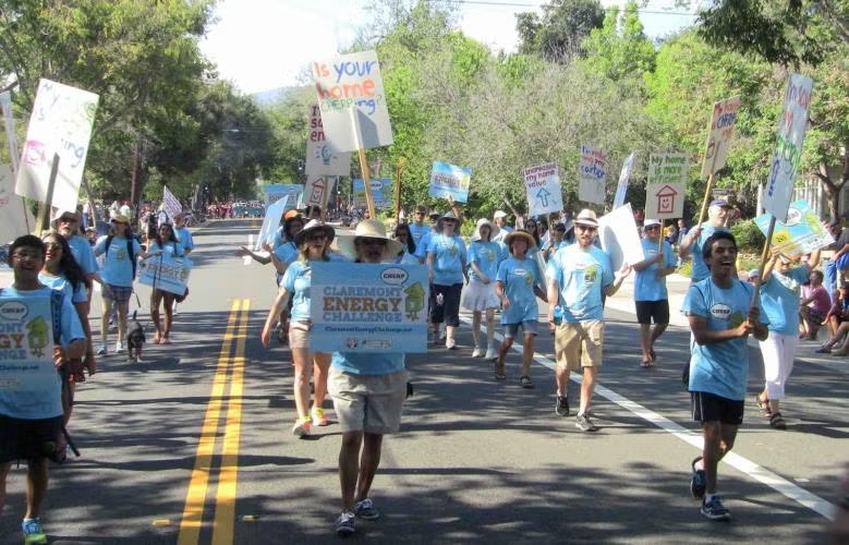 A group of people wearing blue shirts are marching with signs for the Claremont Energy Challenge on a sunny day.