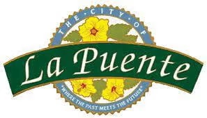 Seal of La Puente city with yellow flowers and green banner stating "La Puente," motto: "Where the Past Meets the Future."