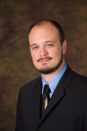 A man in a suit and tie against a blurred brown background.