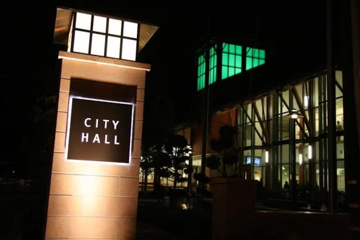 Night view of a building with a lit-up sign reading "City Hall" next to it.
