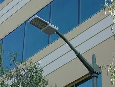 A streetlight in front of a modern building with reflective blue windows and some tree branches.