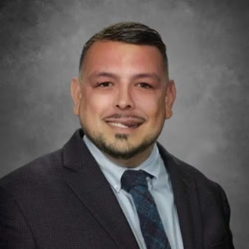 Smiling person in a suit and tie against a gray background.