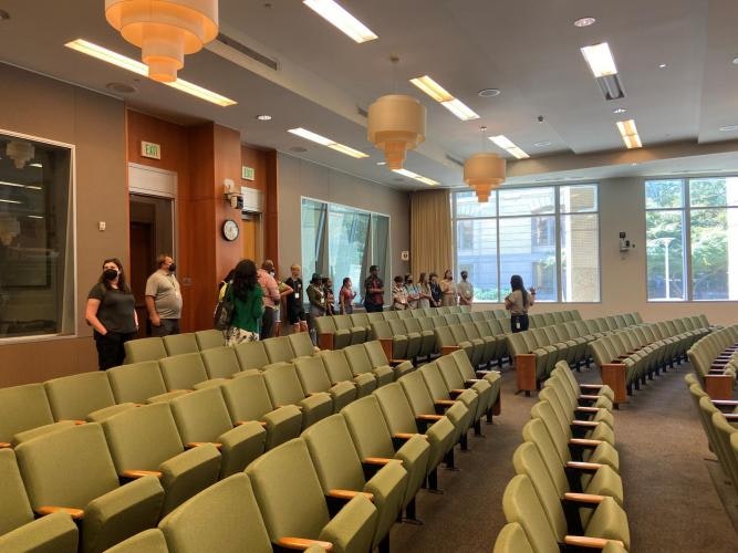 People line up in a lecture hall with green seats and large windows.