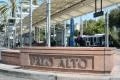 Palo Alto train station platform with passengers, shaded awning, and nearby greenery.