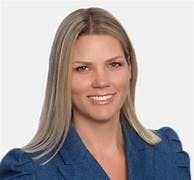 A person with long blonde hair wearing a blue blazer, smiling at the camera.