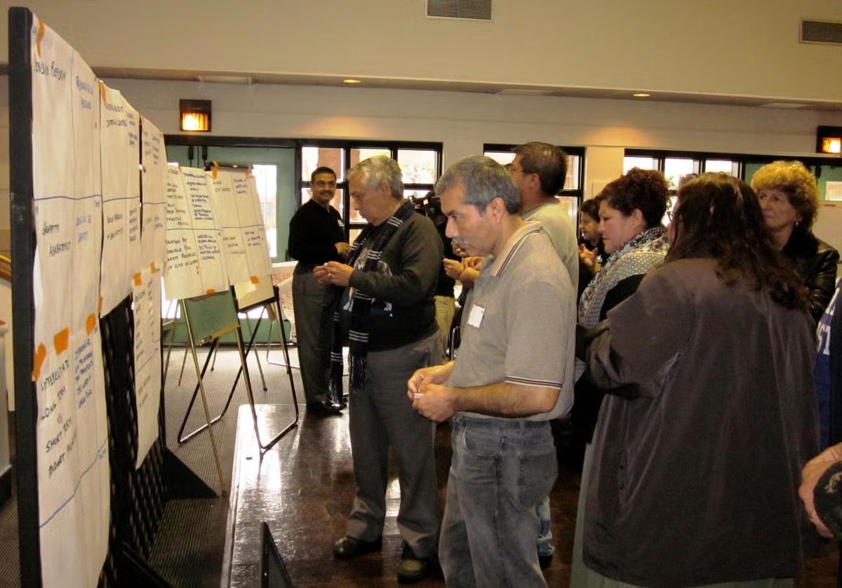 People are gathered around display boards, which have sheets of paper with text, in what appears to be a workshop or meeting.