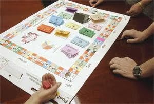 People playing a board game with stacks of colorful cards and pieces on a table.
