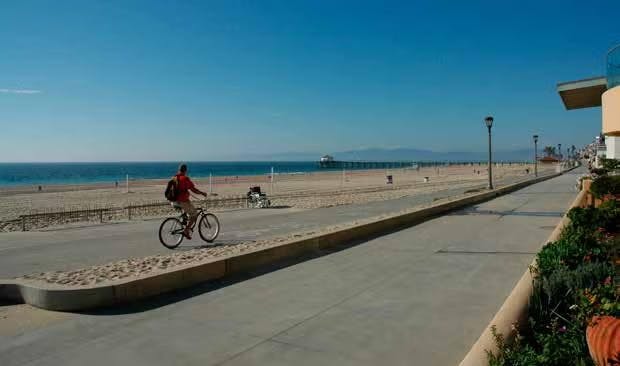 A person rides a bike on a beachside path next to the ocean under a clear blue sky.