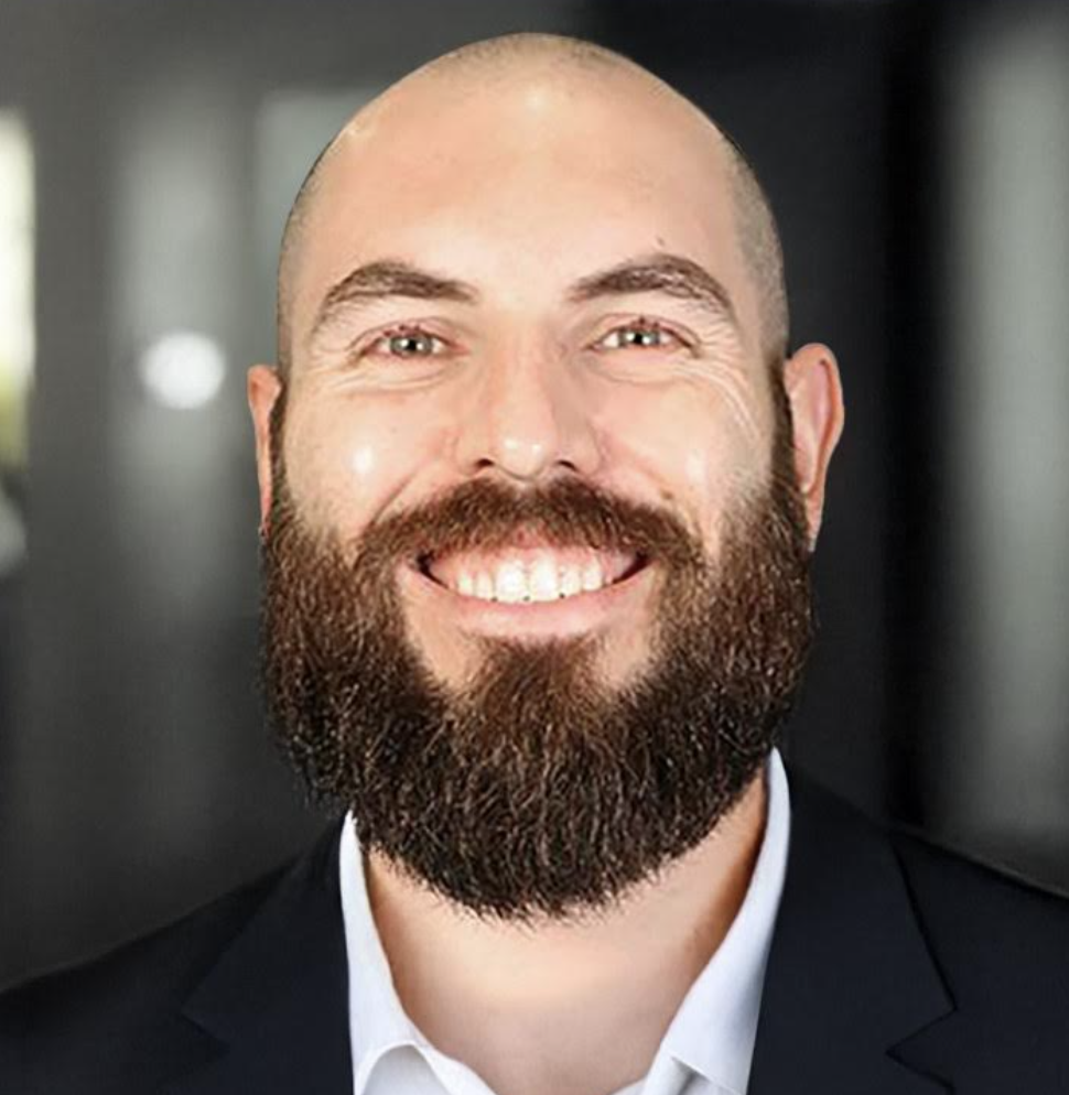 A smiling bald man with a full beard wearing a suit and white shirt.
