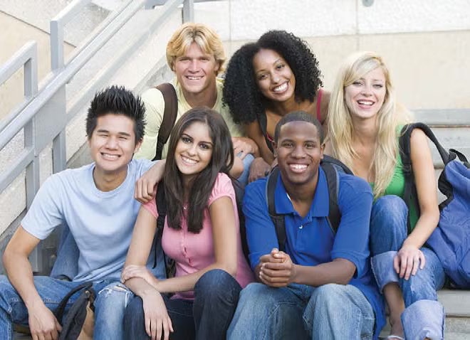 A group of six people sitting on stairs, smiling, with backpacks.