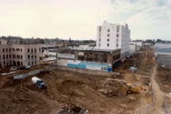 A construction site with dirt, vehicles, and nearby buildings in an urban setting.