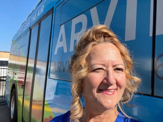 A woman smiling in front of a blue bus with text "Let's Clear the Air."