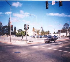A street intersection with traffic lights, trees, a blue sky, and a car turning.