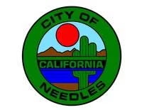 Seal of the City of Needles, California, featuring a cactus, sun, mountains, and a river within a green circular border.