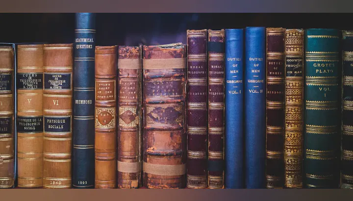 A row of vintage leather-bound books with ornate spines and titles visible.