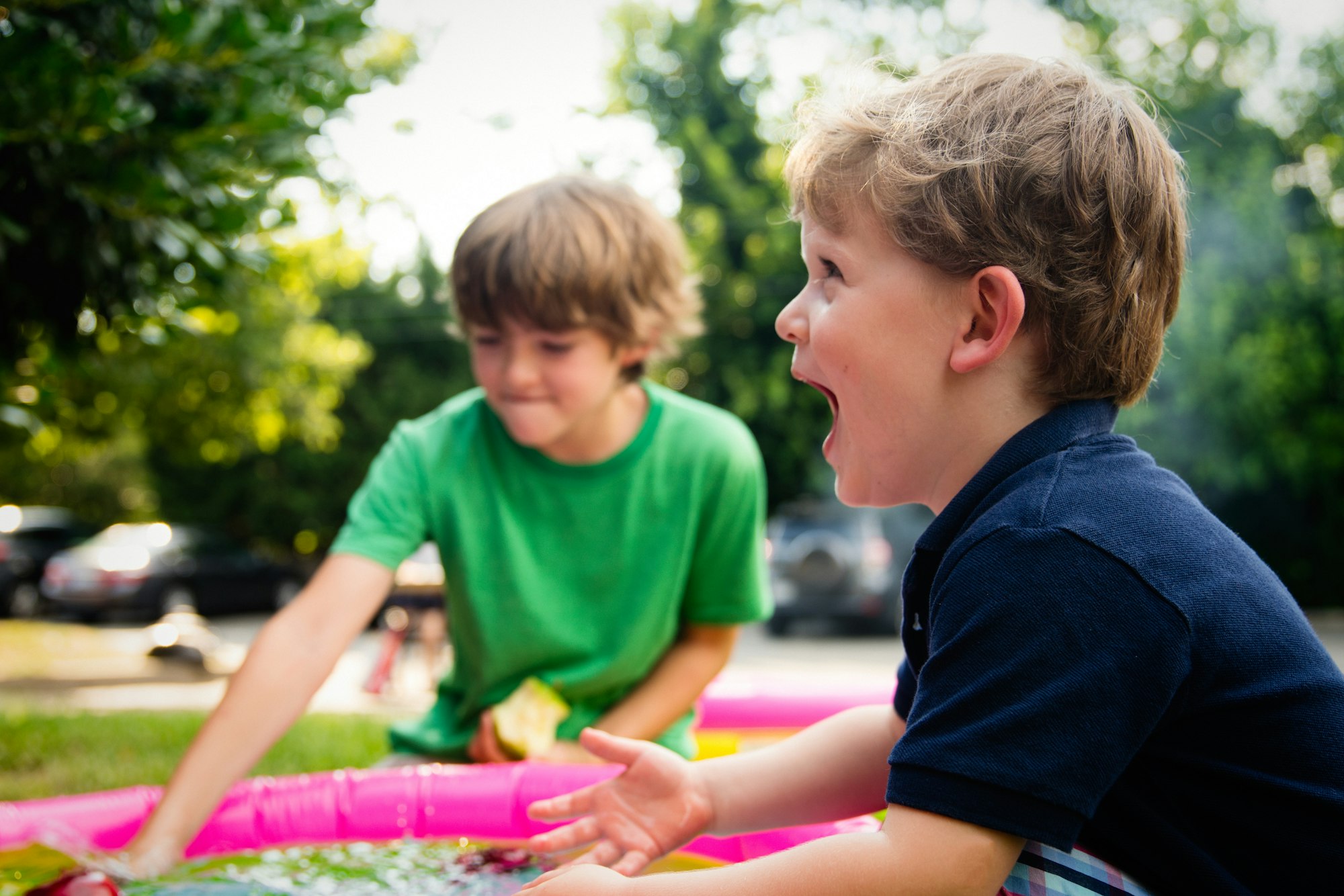 Two boys playing and laughing outdoors on a sunny day, with a colorful water toy in the foreground.
