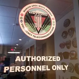 A sign reads "AUTHORIZED PERSONNEL ONLY" below a 911 emergency telecommunications emblem.