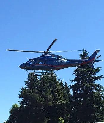 A blue medical helicopter in flight against a clear sky with trees below.