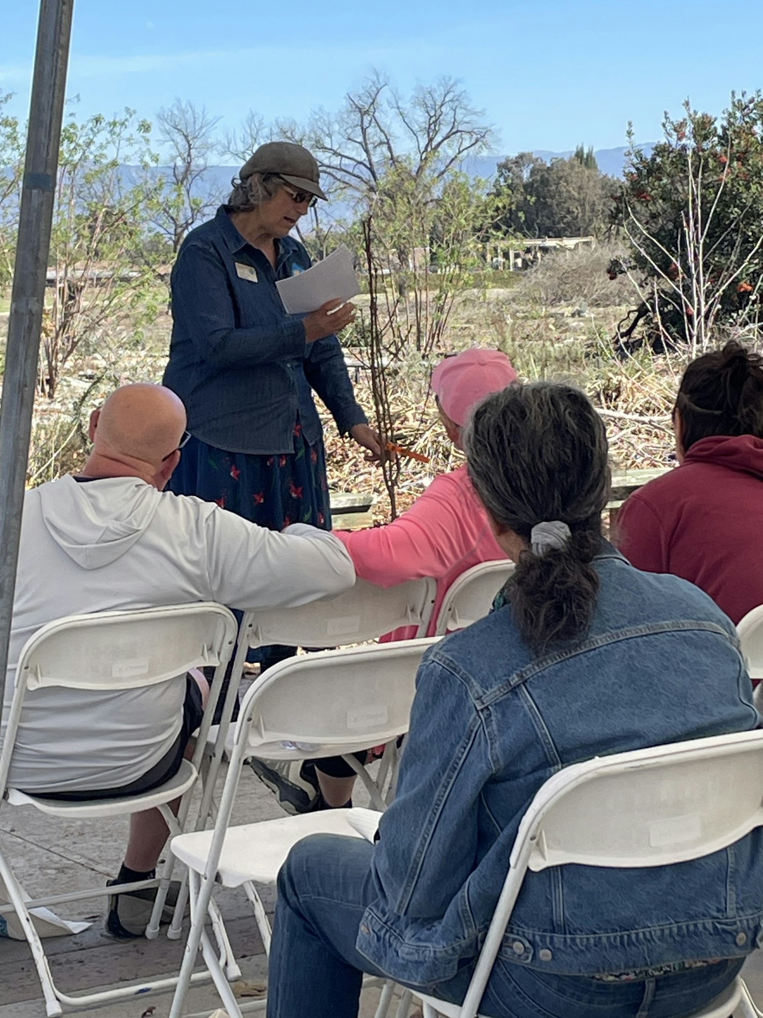 A person is giving a presentation outdoors to a seated audience.