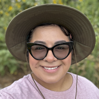 A person wearing a hat and sunglasses, smiling outdoors.
