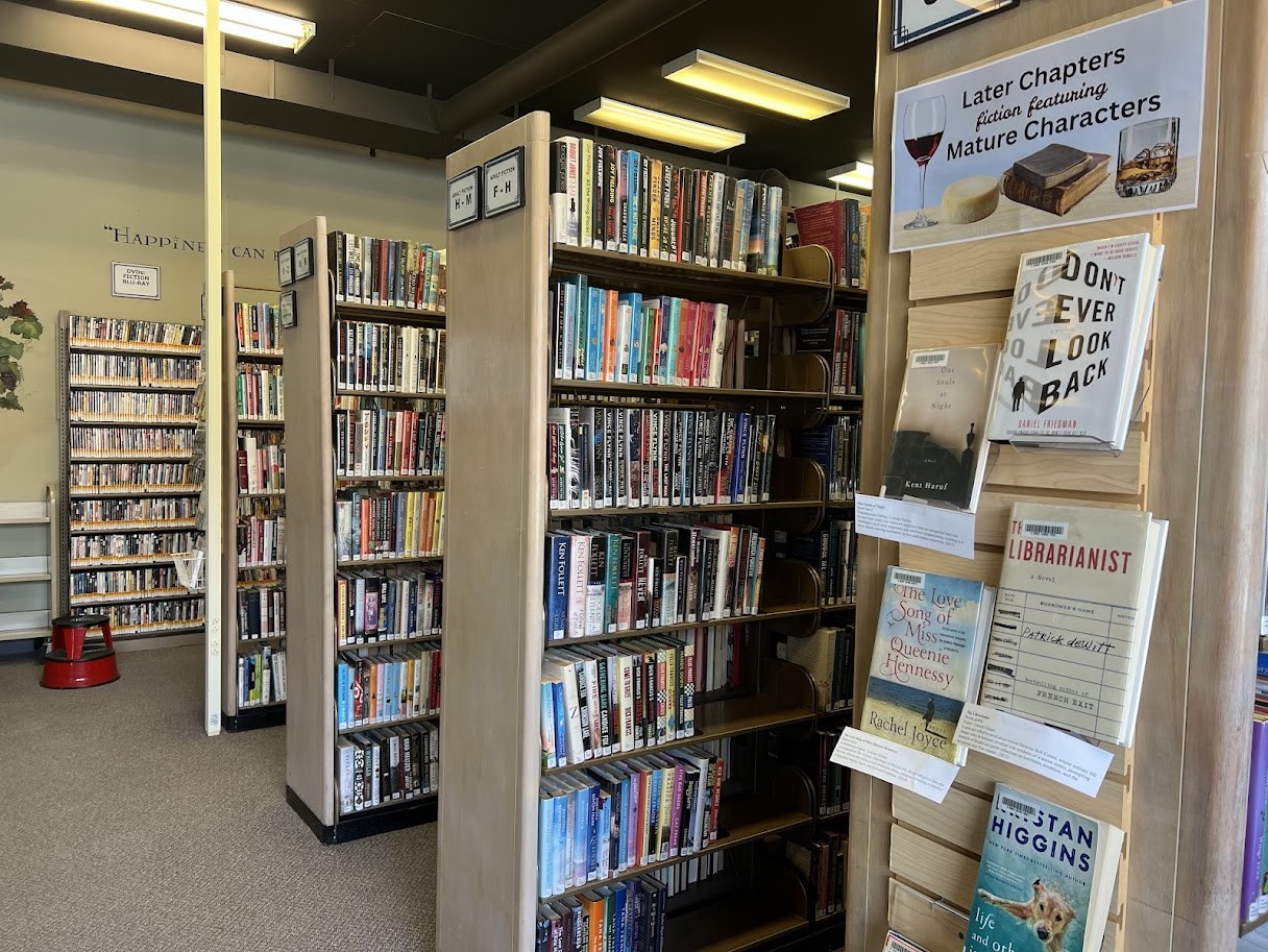 A cozy library scene with shelves of books and a sign for "Later Chapters" featuring mature characters.