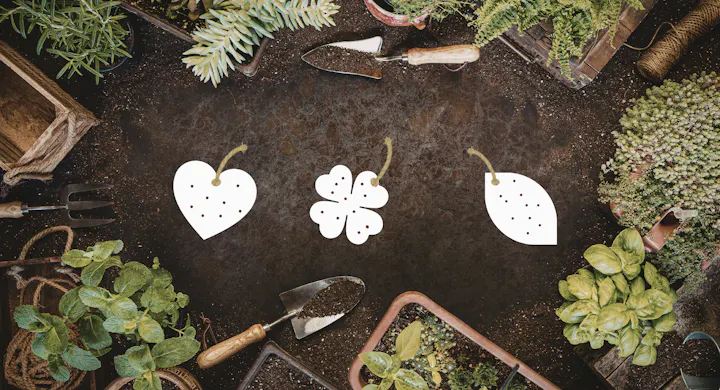 The image shows a gardening scene with tools, plants, and illustrated tags in shapes of a heart, clover, and leaf.