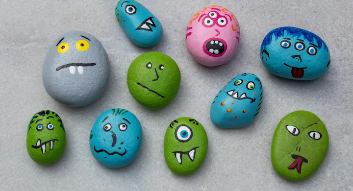 A collection of painted rocks featuring various colorful, cartoonish monster faces with different expressions.