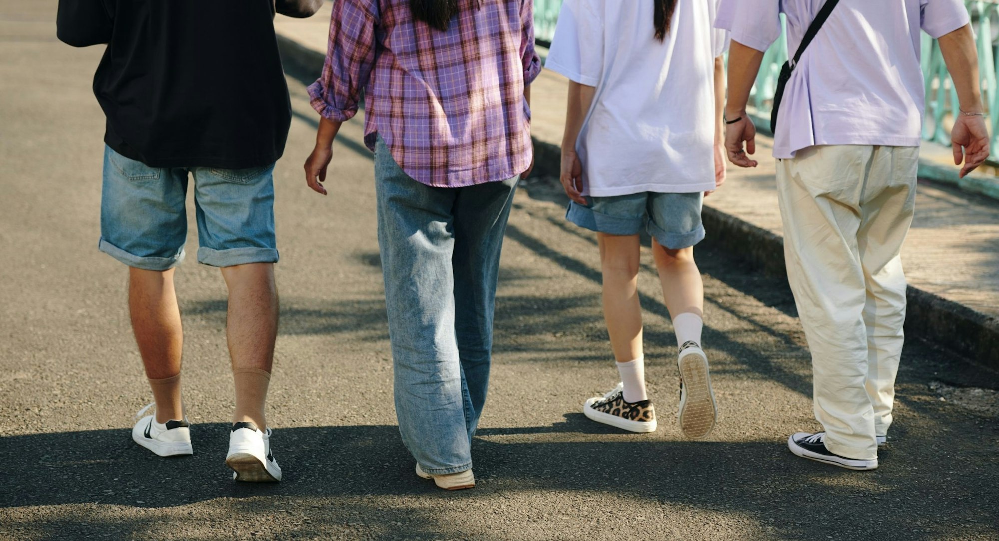 Four people are walking together on a path, wearing casual outfits with shorts and various styles of shoes.
