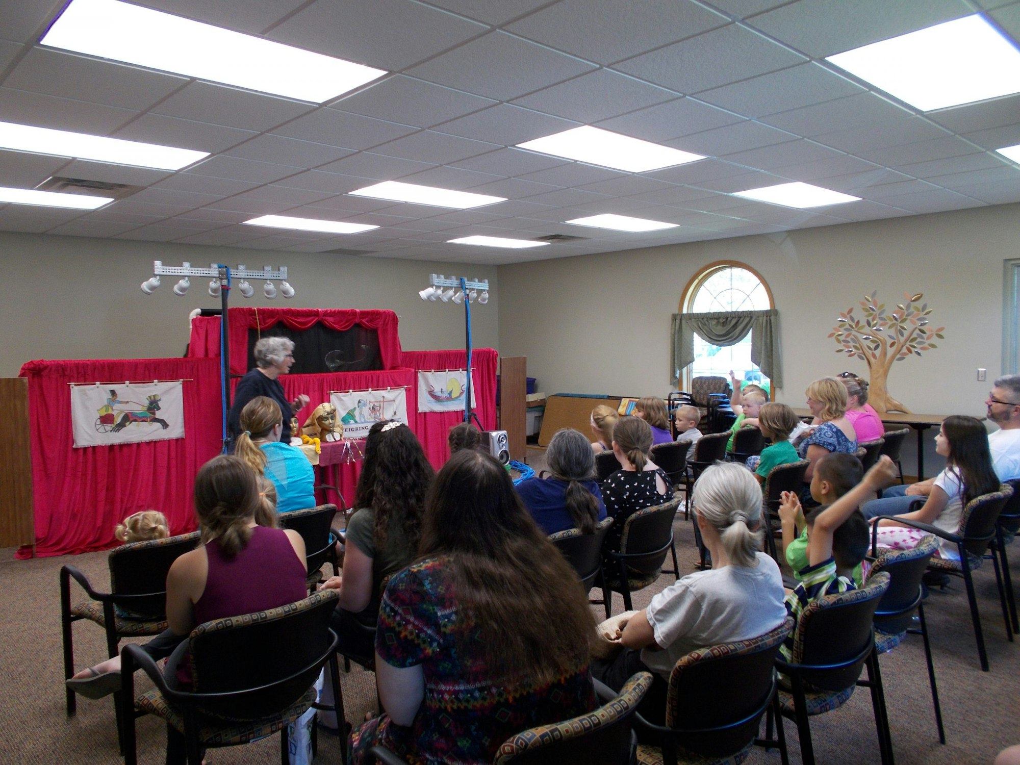 A puppet show is taking place, with children and adults sitting in an audience, engaged and watching the performance.