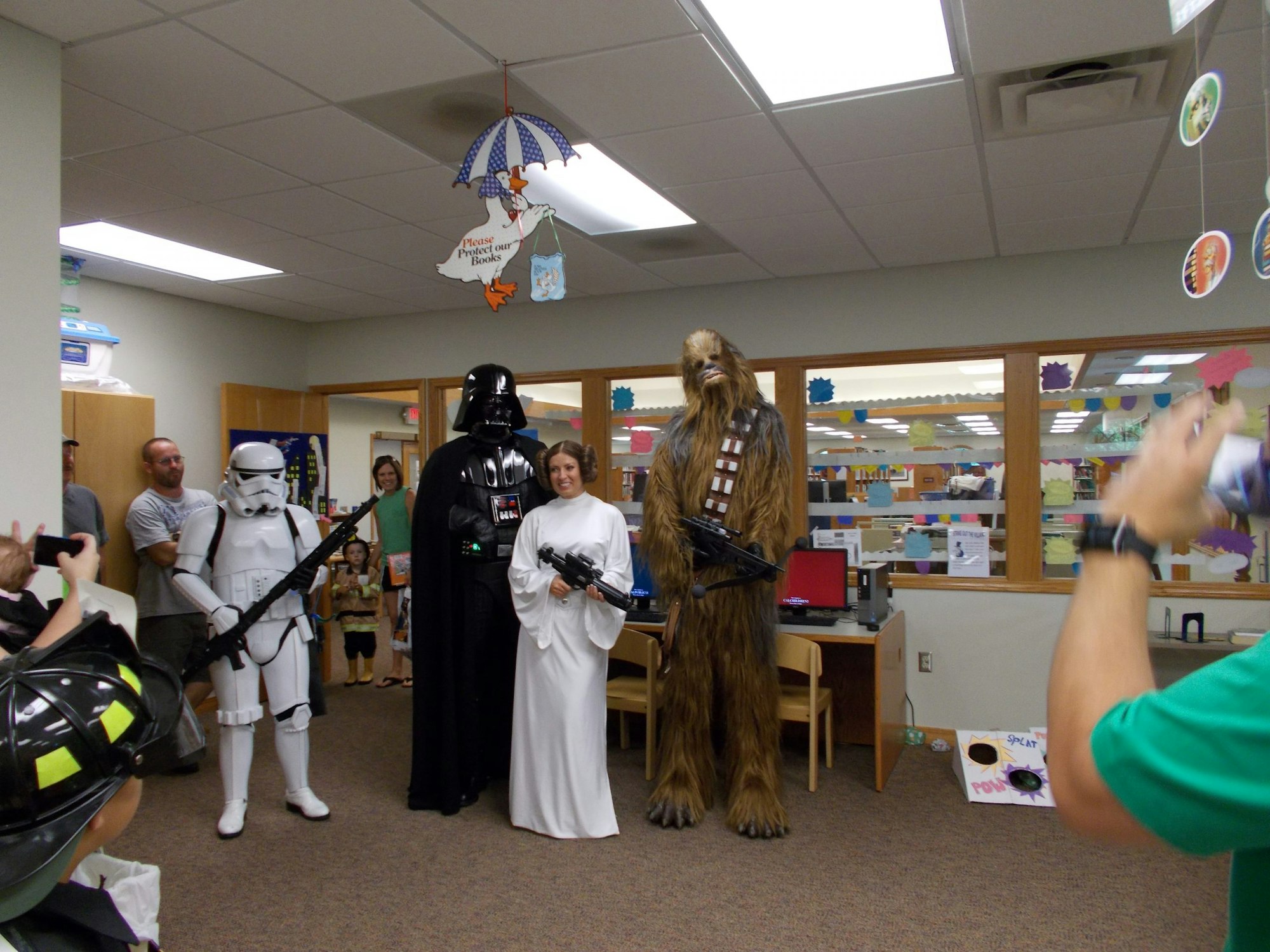 A group dressed as Star Wars characters, including Darth Vader, Chewbacca, and Princess Leia, poses in a library.