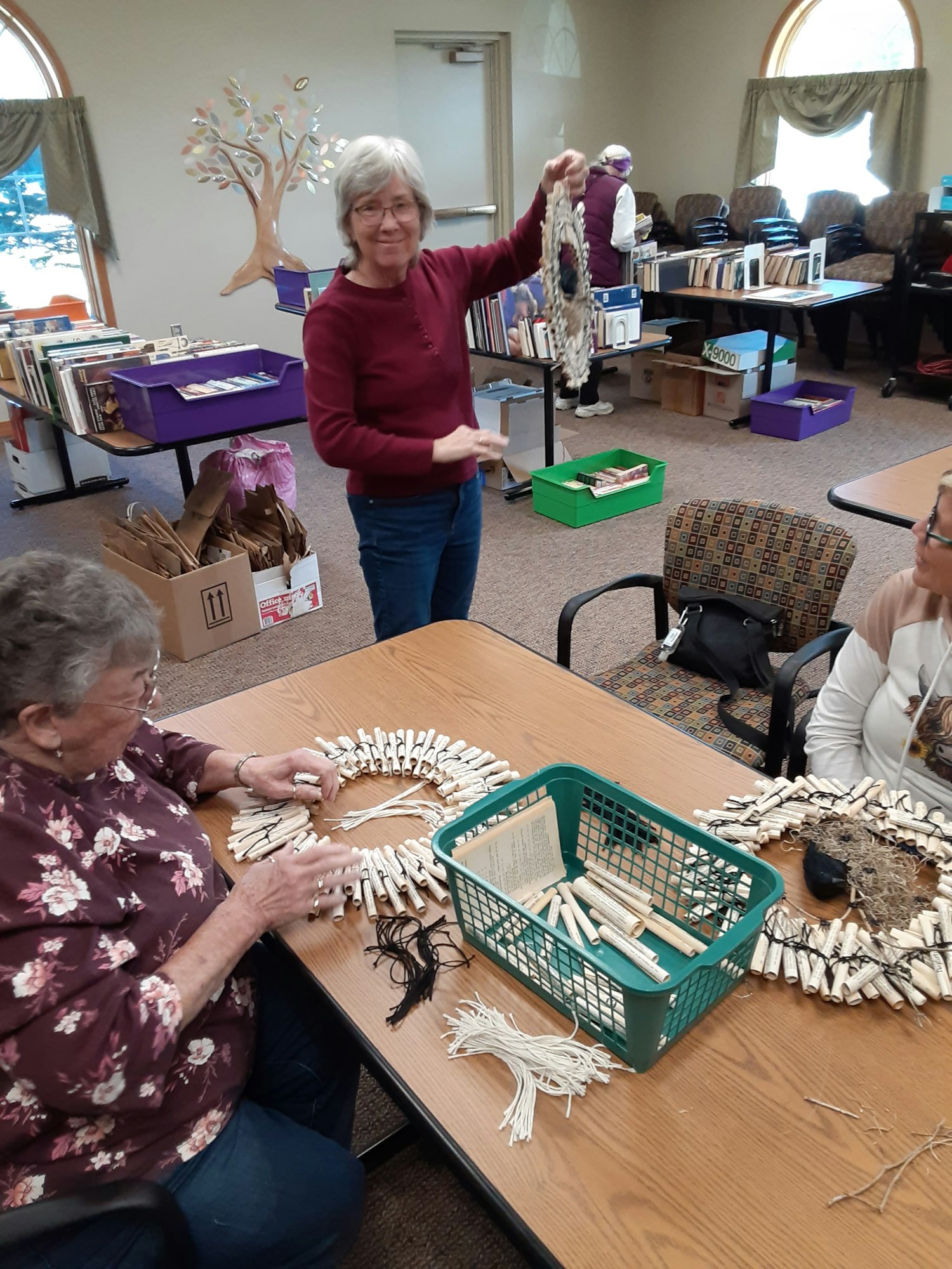 A group of people engaged in a crafting activity, creating decorations from natural materials on tables in a community space.