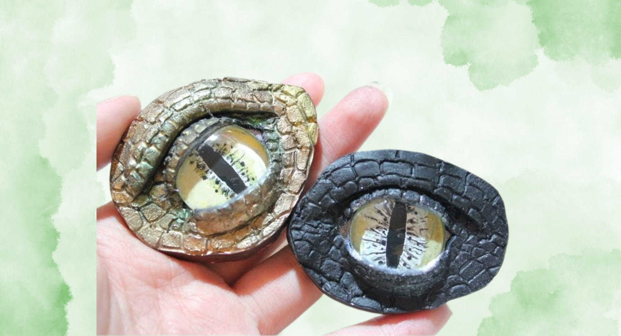 The image shows two decorative reptile eye pieces in gold and black colors held in a hand.